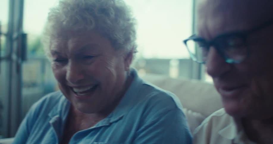 Elderly couple sitting in an armchair and interacting with a tablet