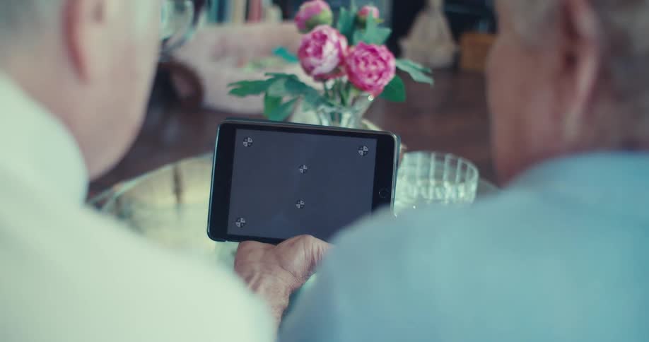 An elderly couple looks at a blank tablet screen together at a table with flowers