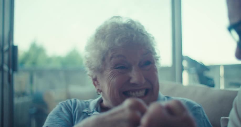 An older adult holds a tablet while sitting on a couch with another person and they celebrate
