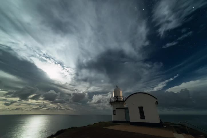 Clouds flowing over a lighthouse and ocean waters
