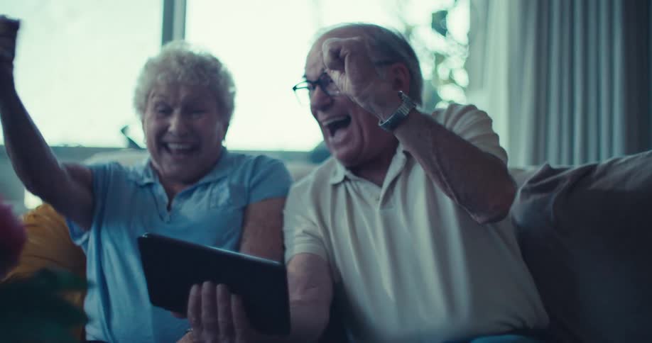Two happy seniors sitting and interacting with a tablet in the living room