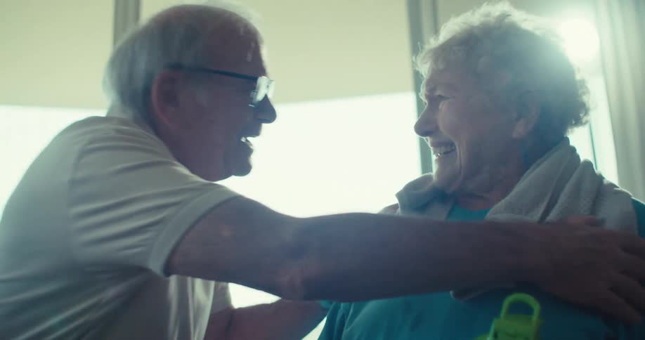 Two elderly people warmly smile at each other in a bright indoor setting