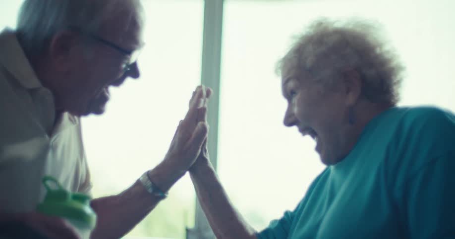 An elderly man and woman laugh and clasp hands while outside