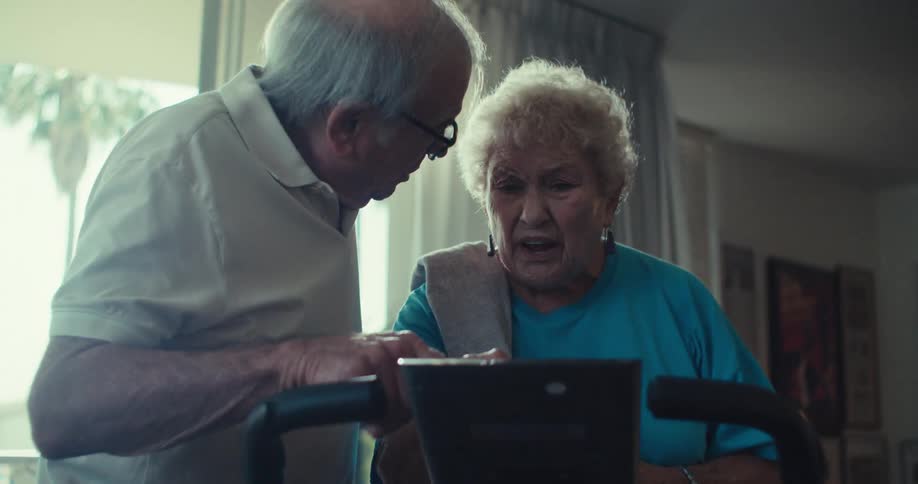 Elderly couple talking and interacting with an exercise bike in a living room