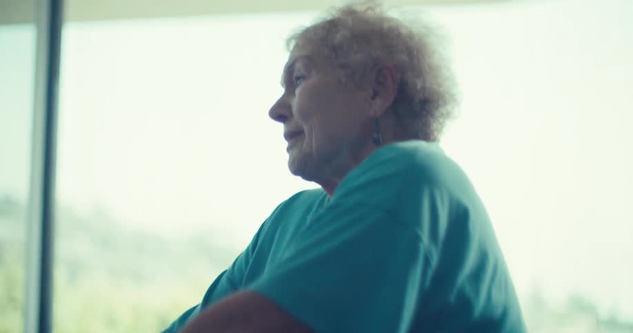 Elderly woman riding an exercise bike in the living room accompanied by a person