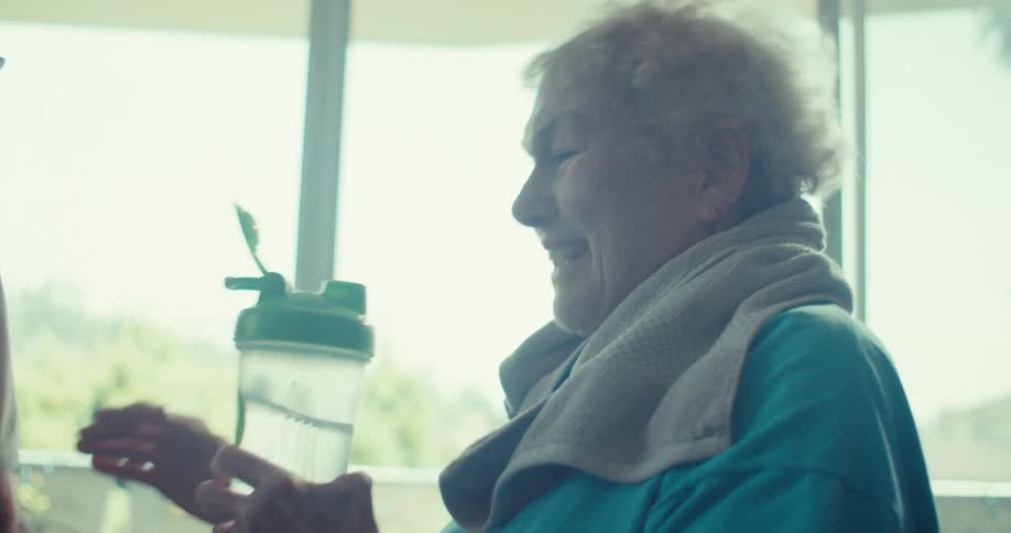 An elderly couple laughs as the woman playfully drinks from a water bottle