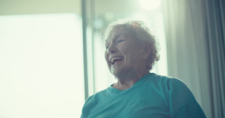 Elderly lady accompanied by another elderly man doing exercise bike in the living room