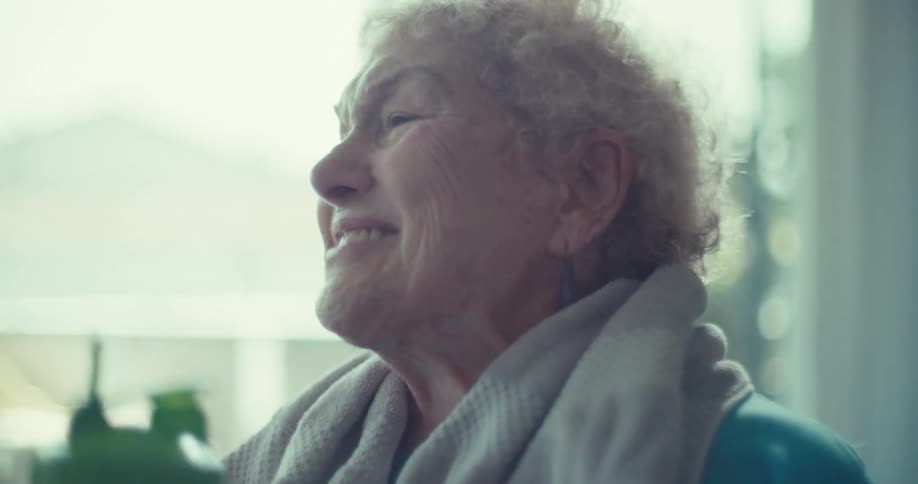 An elderly woman laughs joyfully with a towel around her neck talking to a man