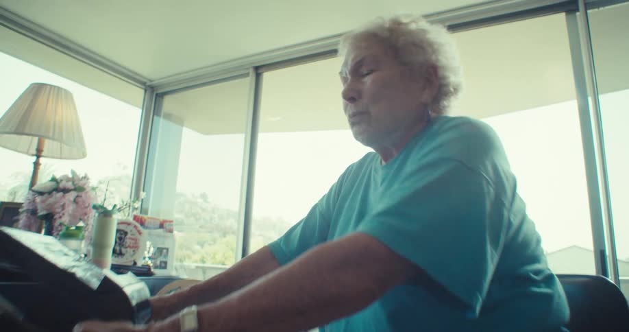 Elderly woman smiles while exercising on a stationary bike in her cozy living room