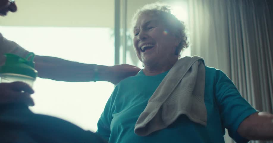 Older man helps woman with an exercise bottle while they both laugh warmly