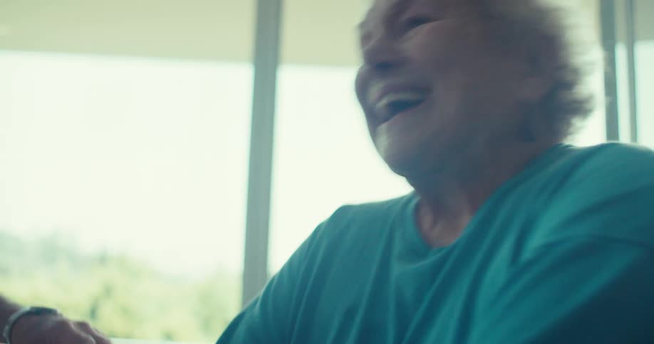Elderly man motivating an elderly lady who is cycling on an exercise bike in the living room