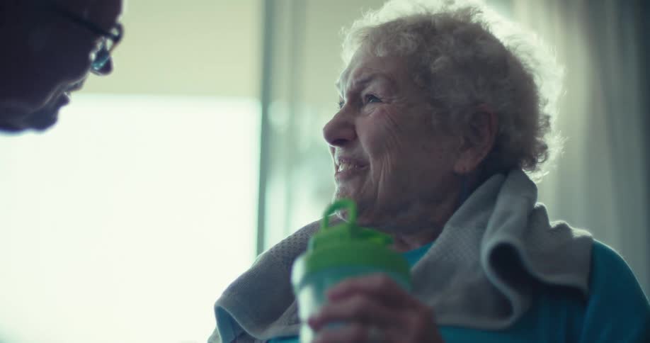 An elderly woman smiles at a man warmly while holding a green water bottle