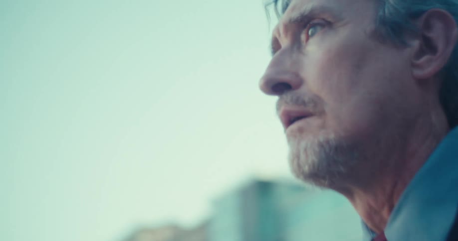 A man in a suit looks ahead with sad focus city buildings blurred in the background