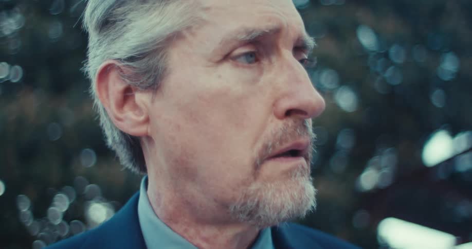 A man in a suit looks to the side with a serious or concerned expression
