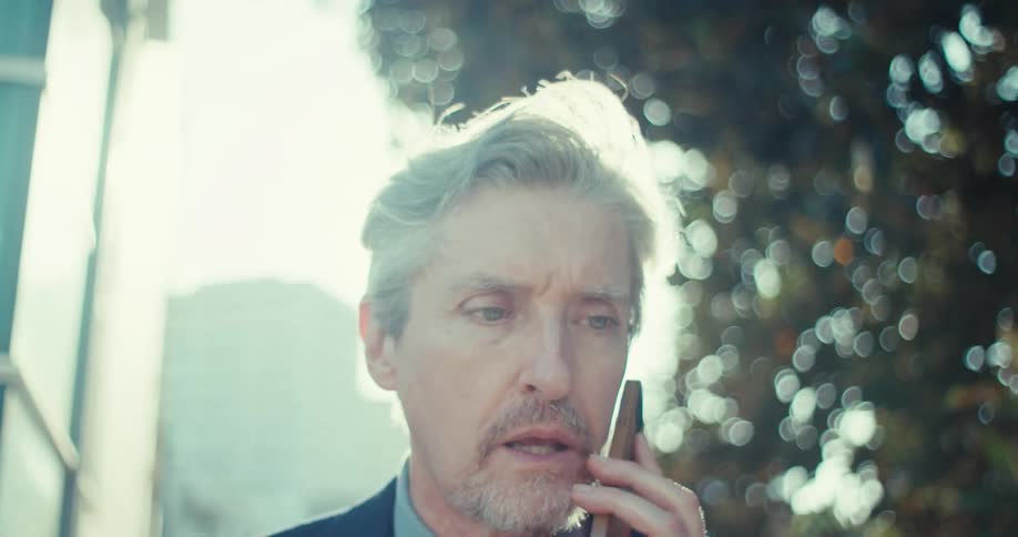 A concerned man is on a phone call in bright daylight