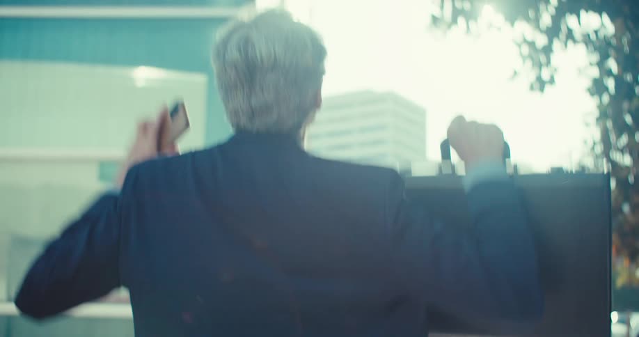 A man in a suit raises his arms joyfully while holding a briefcase outdoors