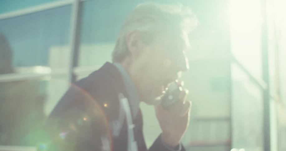 Businessman standing outside a building on a bright sunny day expresses pleased surprised during a phone call