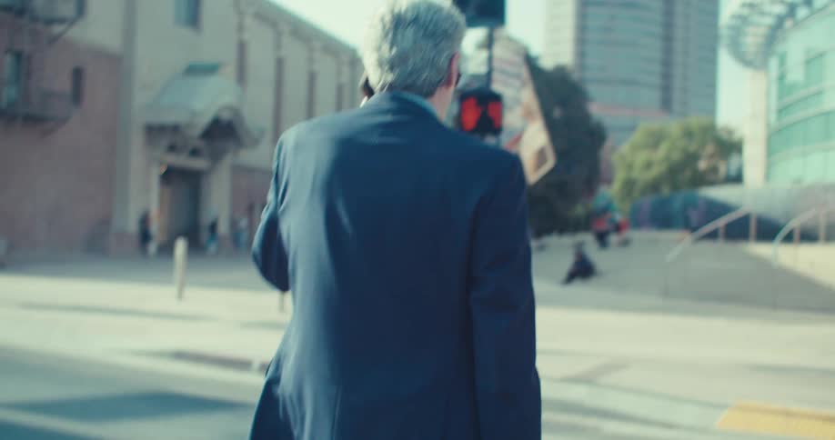 Man in suit on phone call walking across the street in city