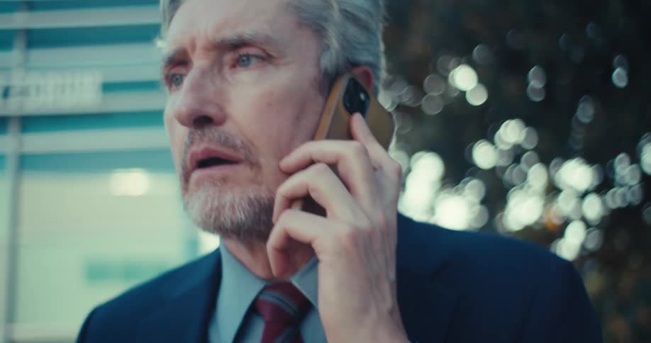 Close up of a middle aged businessman reacting emotionally on a phone call while walking outdoors in a metropolitan city during daytime