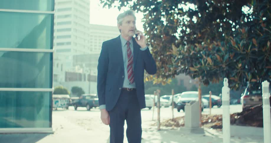 A businessman stops to take an emotional phone call while walking in an urban city during daytime