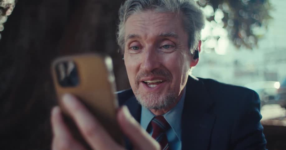 Man in a suit talking animatedly in front of a smartphone