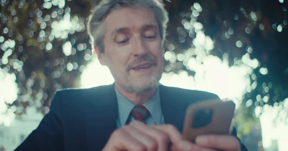 Smiling man in a suit looks at his phone outdoors