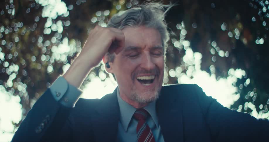 Man with headphones sitting under a tree and happily talking