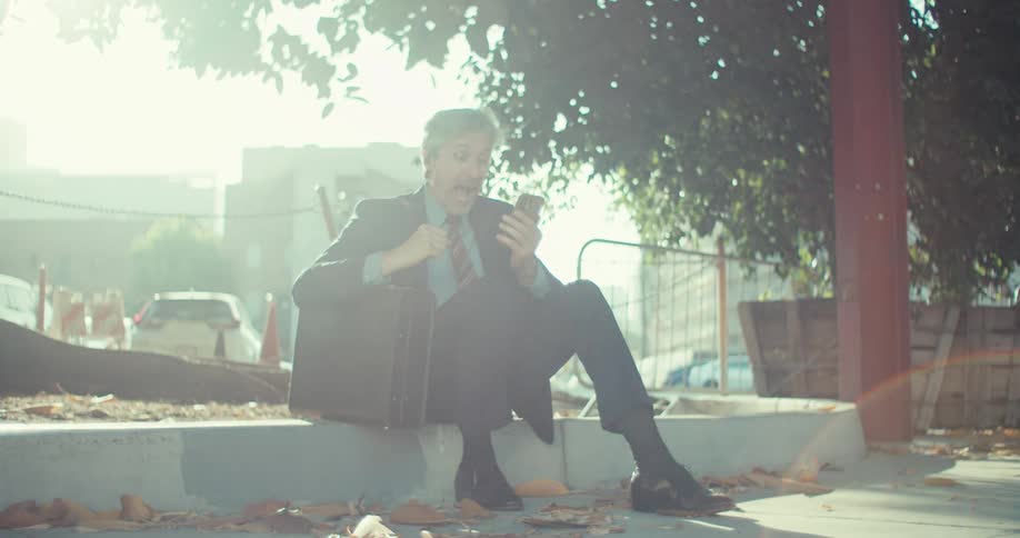 Man sitting outdoors happily reacting to good news on a phone call