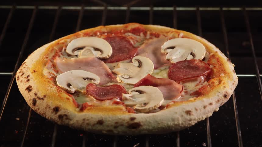 A pizza is baking in an oven with visible toppings like mushrooms and pepperoni