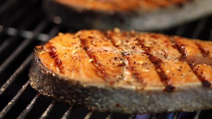 Seasoned salmon steaks sizzle on a grill with perfect sear marks