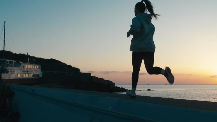 Woman jogging along the coast at sunset