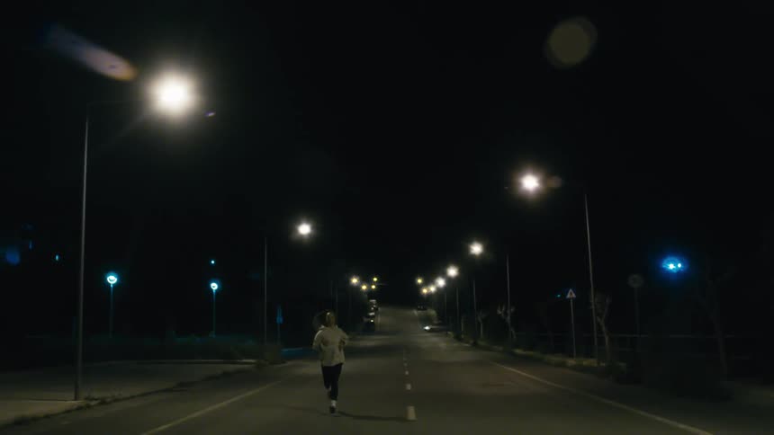 Person jogging alone on an empty road at night under streetlights