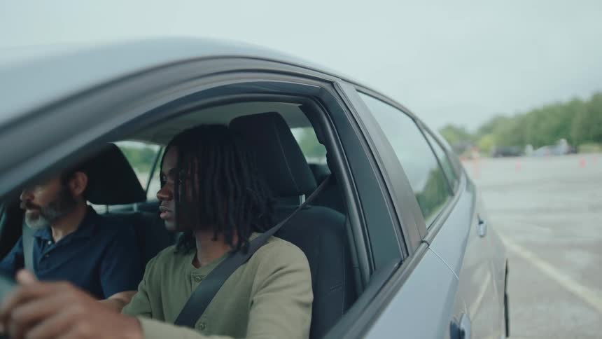 A driving instructor and student sit in a car focused on learning