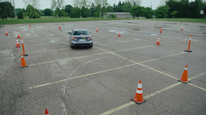 A car navigates a driving course in an empty parking lot lined with traffic cones