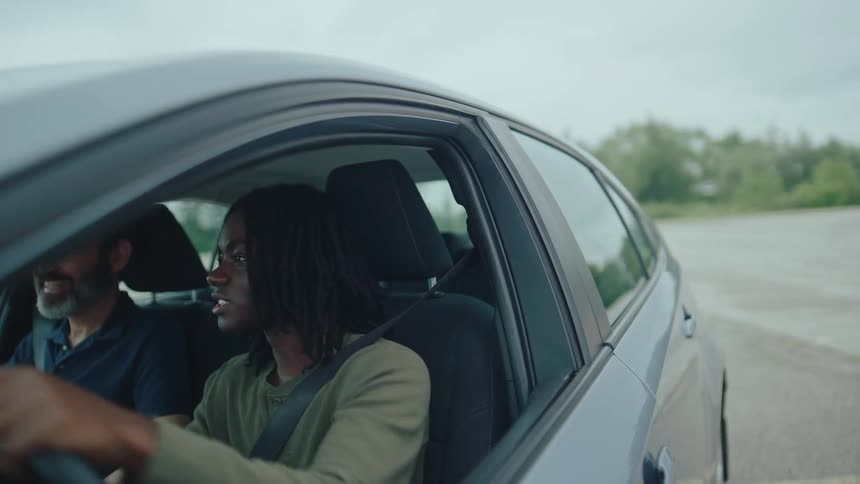 Young man learns to drive with instructor in parked car