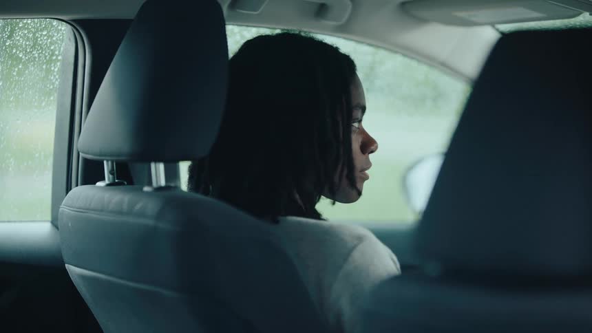A girl is sitting in the car as it rains