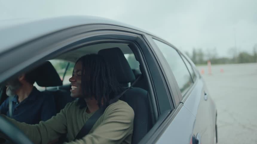 Man accompanied by an examiner driving a vehicle between cones