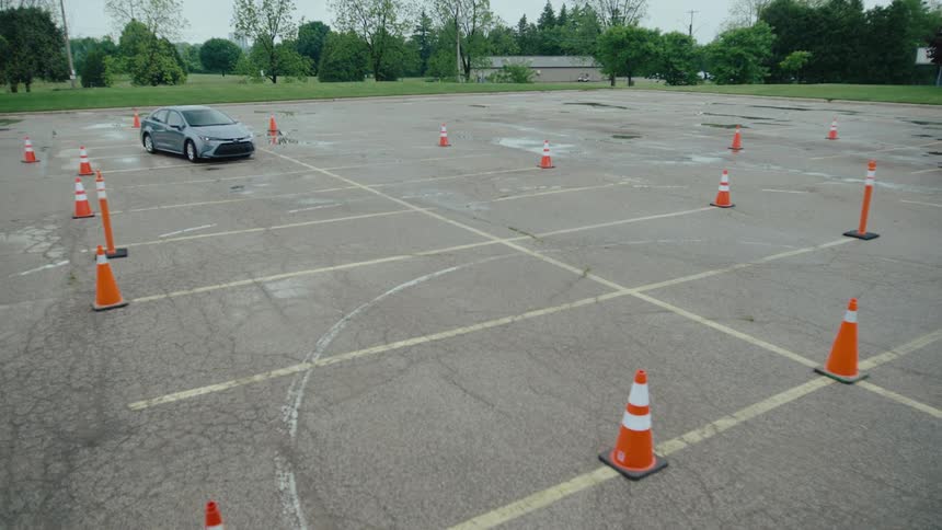 Traffic cones mark a driving course in an empty wet parking lot and a driver is driving and parks
