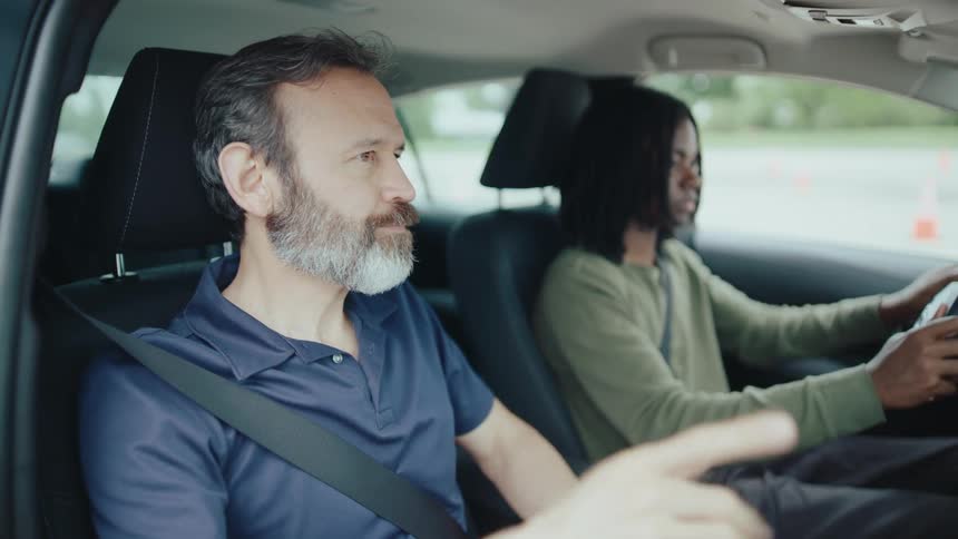 Instructor teaching a person next to him how to drive a car