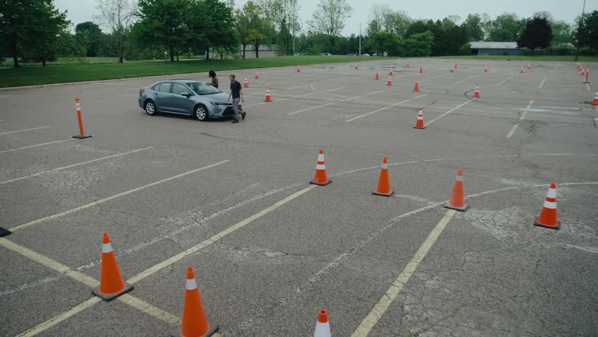 A person is getting into a parked car surrounded by traffic cones in an empty lot