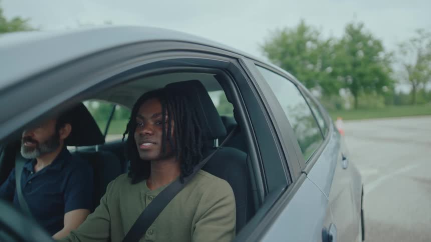 The teenager is smiling and turning the car during a driving lesson