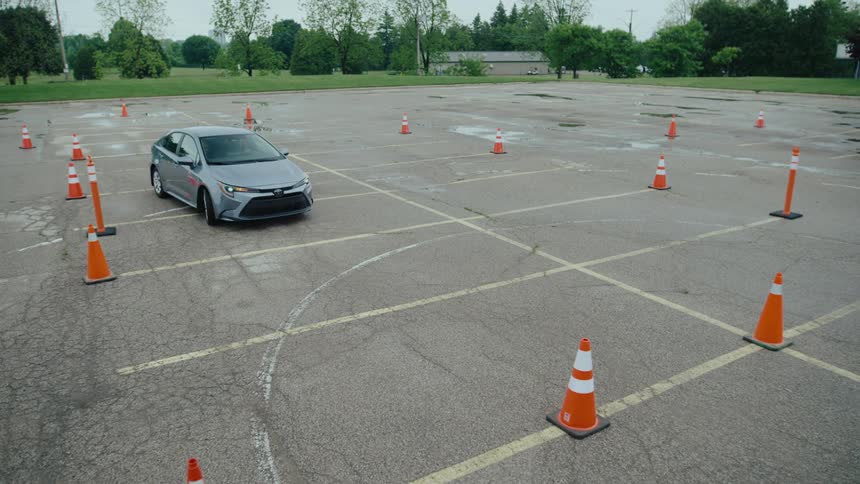 A silver car navigates through a conemarked driving course in a large lot