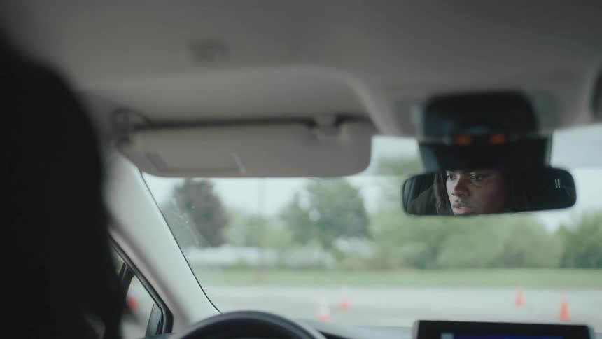 A mans serious face is reflected in the rearview mirror during a car ride