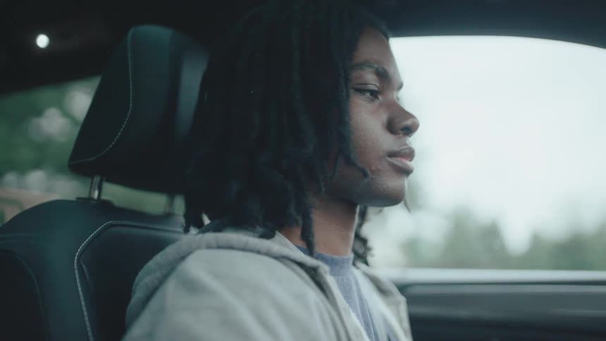 A young male sits down in the driver seat of a car and starts driving