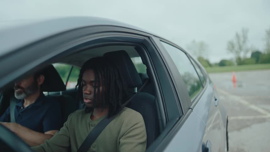 Anxious teenage student driver learning to drive with an unhappy instructor in a parking lot