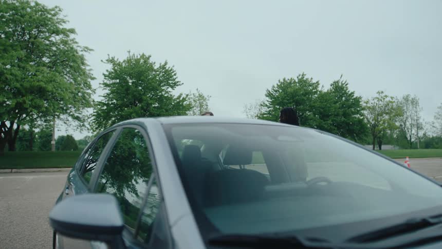 Two men standing beside a car during a driving lesson or discussion in an outdoor setting