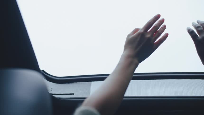 Hands waving out of sunroof while driving in a car
