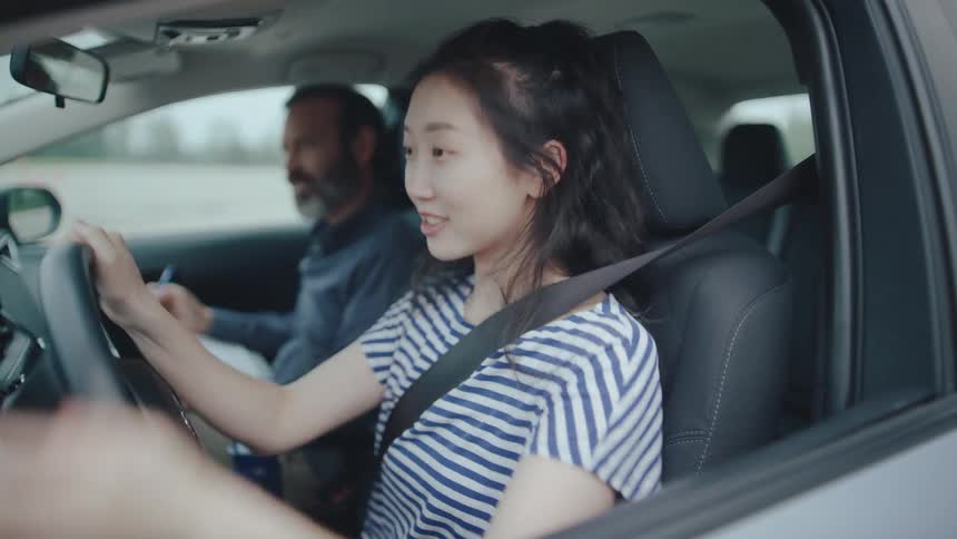 Young asian woman steers a vehicle while practising driving with a male instructor during daytime