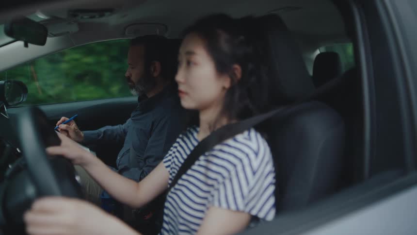 Young woman learning to drive with instructor beside her
