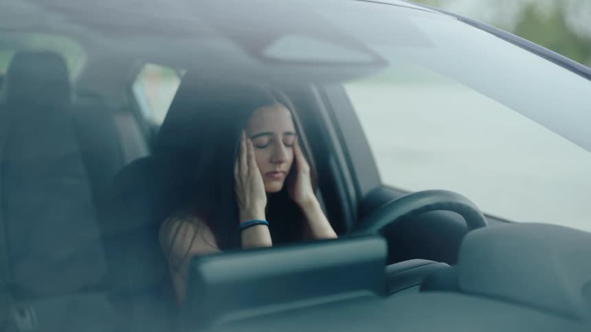 A woman sits in a car covering her face in distress